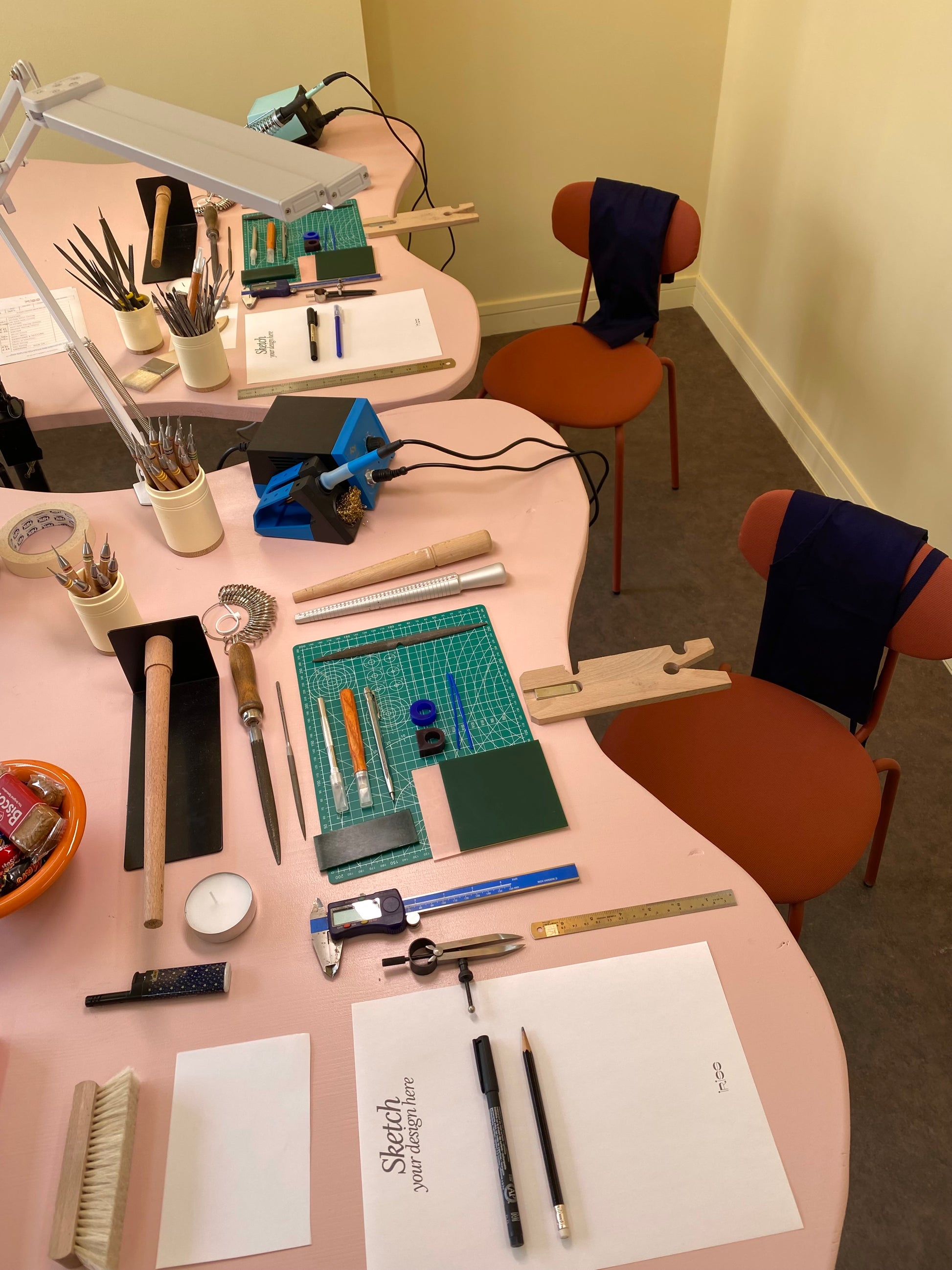 Workshop setup with tools and materials on a pink table, including rulers, pencils, and a lamp.