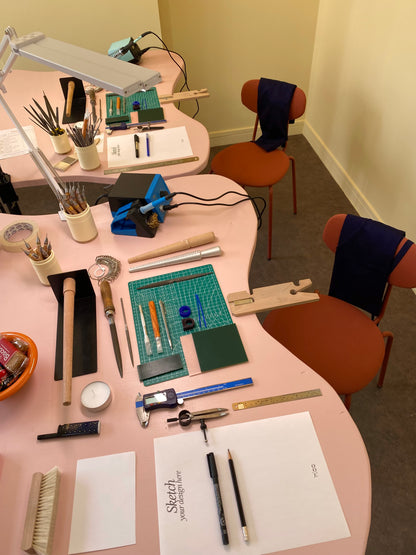 Workshop setup with tools and materials on a pink table, including rulers, pencils, and a lamp.